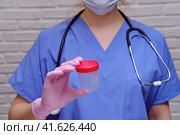 A nurse in protective gloves is holding an empty test jar. Doctor in a medical uniform with a plastic container for urine, close-up. Стоковое фото, фотограф Андрей Журавлев / Фотобанк Лори