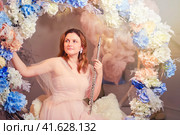 Smiling woman sits with a flute on a swing in flowers. Studio portrait of happy woman musician in pink dress. Стоковое фото, фотограф Андрей Журавлев / Фотобанк Лори
