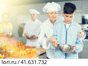 While childrens cooking class, female chef helps teen boy stir homogeneous dough with whisk. Стоковое фото, фотограф Яков Филимонов / Фотобанк Лори