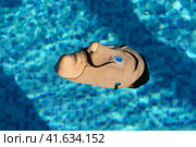 Moscow region, Russia - March 17, 2023: Salvador Dali mask is lying on the blue water surface in the swimming pool. Blue water background. Bright sun. Abstraction. Close up  image. Редакционное фото, фотограф YuryKara / Фотобанк Лори