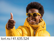 An African young man in a yellow jacket shows a thumbs-up against a blue sky. Generated by Ai. Стоковое AI-изображение, AI-художник Ярославский Максим / Фотобанк Лори