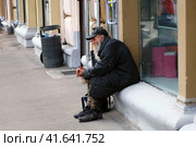 A homeless old man with a beard sits outside a store. An empty street because of the quarantine in the coronavirus epidemic, the problem of strays in the pandemic - May 12, 2020, Moscow, Russia. Редакционное фото, фотограф Андрей Журавлев / Фотобанк Лори