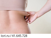 Woman holding fold of skin, cellulite on female body, beige background. Стоковое фото, фотограф Станислав Тарко / Фотобанк Лори