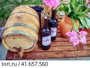 Moscow \ Russia 06 07 2019: Wooden barrel, flowers and wine bottles with a retro style label. American wine of the conquest of the wild West - PortWine, George Storm, Hudson N. Y. Редакционное фото, фотограф Андрей Журавлев / Фотобанк Лори