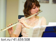The girl plays a large silver transverse flute. A woman in white dresses blows a orchestral flute at a concert. In the hands of the musician metal musical instrument. Стоковое фото, фотограф Андрей Журавлев / Фотобанк Лори