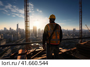 A mature engineer on a construction site in a protective vest and helmet, looking down from a height at the construction site. Generated by AI. Стоковое AI-изображение, AI-художник Ярославский Максим / Фотобанк Лори