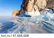 Frozen Baikal Lake on sunny cold winter day. View of Cape Sagan-Khushun - natural landmark of Olkhon Islands from ice field with hummock. Chunks of blue ice floes near rocks covered with crust of ice. Стоковое фото, фотограф Виктория Катьянова / Фотобанк Лори
