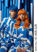 A young smiling cheerful couple, two friends, a family man and a woman in unusual blue designer clothes, stand next to each other, directing their gaze at the camera. Generated by AI. Стоковое AI-изображение, AI-художник Ярославский Максим / Фотобанк Лори