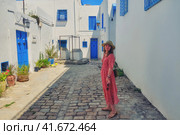A young woman stands in the courtyard with blue windows and doors with Arabic ornaments. Texture of Islamic symbols in Sidi Bou said, Tunisia, Africa (2019 год). Стоковое фото, фотограф Андрей Журавлев / Фотобанк Лори