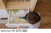 Toddler baby opened the cabinet drawer with pills and medicine. Child boy holding a pack of pills in the home living room. Kid aged about two years (age one year nine months) Стоковое видео, видеограф Андрей Журавлев / Фотобанк Лори