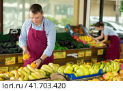 Male seller of vegetable department of store is replenishing showcase with oranges. Стоковое фото, фотограф Яков Филимонов / Фотобанк Лори
