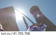 A young woman with long flowing hair, in an oriental robe and skullcap, holds an Asian saber against the backdrop of an ancient city. Slow Motion. Стоковое видео, видеограф Aleksey Kidisyuk / Фотобанк Лори