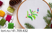 Winter crafts.Video of branches of Christmas tree with colorful balls are embroidered using long stitch technique in wooden hoop. Skeins of colored threads and needle bed. Handmade New Year gifts. Стоковое видео, видеограф Виктория Катьянова / Фотобанк Лори