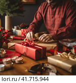 An unrecognizable man wraps Christmas gifts in craft paper. Стоковое AI-изображение, AI-художник Margarita Davchenko / Фотобанк Лори