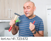 Imposing man holds in teeth of screws and holding hammer. Стоковое фото, фотограф Татьяна Яцевич / Фотобанк Лори