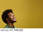A young African man in a T-shirt on a uniform background looks up and smiles. Generated by AI. Стоковое AI-изображение, AI-художник Ярославский Максим / Фотобанк Лори