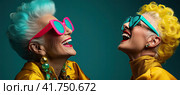 Two elderly beautiful women with brightly colored hair, wearing sunglasses smile and look up on a blue background. Generated by AI. Стоковое AI-изображение, AI-художник Ярославский Максим / Фотобанк Лори