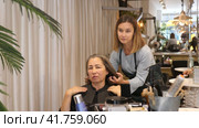Portrait of young woman professional hair stylist talking to elderly female client in salon, choosing new hairdo. Стоковое видео, видеограф Яков Филимонов / Фотобанк Лори