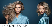Two young beautiful blondes with developing hair stand on a blue background. Young femininity. Стоковое AI-изображение, AI-художник Ярославский Максим / Фотобанк Лори