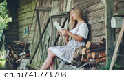 Village Slavic girl flipping a tablet in the countryside by the barn. Стоковое фото, фотограф Mikhail Davidovich / Фотобанк Лори