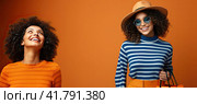 Two beautiful brunette with curly hair in sunglasses posing in front of the camera in a yellow studio. Стоковое AI-изображение, AI-художник Ярославский Максим / Фотобанк Лори