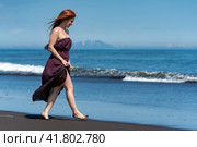 Redhead woman walking sandy beach in long dress with raised hem to her knees, enjoys summer holiday. Стоковое фото, фотограф А. А. Пирагис / Фотобанк Лори