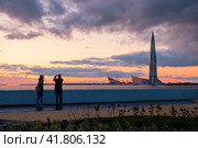 Санкт-Петербург, Россия. Туристы на набережной фотографируют красивый закат над Балтийским морем. Вид на самое высокое здание Европы – небоскрёб Лахта Центр. (2019 год). Редакционное фото, фотограф Андрей Степанов / Фотобанк Лори