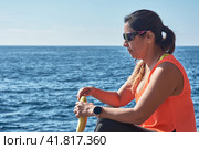 Latin woman, middle-aged, resting, regaining strength, eating, drinking water, after a gym session, burning calories, keeping fit, outdoors by the sea, wearing headphones and smart watch. Стоковое фото, фотограф carlos l vives / Фотобанк Лори