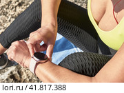 Latin woman, middle-aged, resting, regaining strength, eating, drinking water, after a gym session, burning calories, keeping fit, outdoors by the sea, wearing headphones and smart watch. Стоковое фото, фотограф carlos l vives / Фотобанк Лори