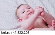 Portrait of a happy infant baby on the bed pulling his leg into his mouth, eight months old. Laughing toddler kid on sofa, face close-up. Стоковое видео, видеограф Андрей Журавлев / Фотобанк Лори