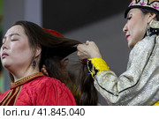 Невесте после свадьбы женщины расплетают девичьи косы и готовят невесту к замужеству во время свадебного обряда по калмыцким традициям на выставке-форуме "Россия" на ВДНХ в городе Москве, Россия (2023 год). Редакционное фото, фотограф Николай Винокуров / Фотобанк Лори