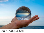 man's hand holds a glass orb lens in which an inverted reflectio. Стоковое фото, фотограф Артем Курутин / Фотобанк Лори