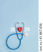 Blue stethoscope, polydiagonal decorative heart and numbers 2024 on pastel background. Concept of health care in the New Year. Selective focus, copy space. Стоковое фото, фотограф Клара Мухаметзянова / Фотобанк Лори
