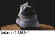 A woman's white sneaker with the inside and back to the camera stands on a wooden surface against a dark background. The camera flies around. Parallax effect. Krasnodar, Russia, April 19, 2022. Редакционное видео, видеограф Воловодов Владимир / Фотобанк Лори
