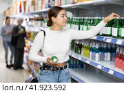 Young female shopper choosing Korean soju bottle at liquor store. Стоковое фото, фотограф Яков Филимонов / Фотобанк Лори