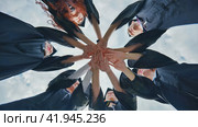 Team of college or university students celebrating graduation. Group of happy successful graduates in academic hats and robes standing in circle and putting their hands together. Стоковое фото, фотограф Mikhail Davidovich / Фотобанк Лори