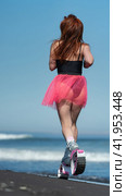 Rear view sportswoman in sports Kangoo Jumps boots, one piece swimsuit and short skirt running and jumping on beach during aerobic session workout (2022 год). Редакционное фото, фотограф А. А. Пирагис / Фотобанк Лори