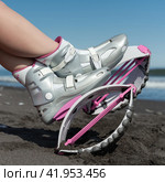 Close-up female legs in trendy Kangoo Jumps boots on sandy beach while resting during aerobic fitness training session workout. Side view sports boots (2022 год). Редакционное фото, фотограф А. А. Пирагис / Фотобанк Лори
