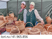 Caucasian women in stylized Russian outfits selling wicker baskets at Traditional Irbit fair, Russia (2023 год). Редакционное фото, фотограф Ирина Кононова / Фотобанк Лори