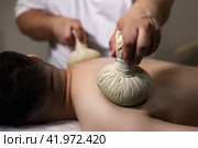 Close-up of masseur doing massage for back guy with herbal compresses bag Thai method. Relaxing spa massage of man back at salon, health herb massaging. Relax spa massaging concept. Copy ad text space. Стоковое фото, фотограф Aleksandr Golubev / Фотобанк Лори