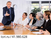 Angry elderly male boss scolding office workers of different ages using notebooks at table in office. Стоковое фото, фотограф Яков Филимонов / Фотобанк Лори