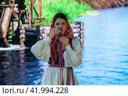 Девушка в русской народной одежде скручивает тесьму со славянским орнаментом на стенде Орловской области  во время проведения выставки-форума "Россия" на ВДНХ в городе Москве, Россия (2024 год). Редакционное фото, фотограф Николай Винокуров / Фотобанк Лори