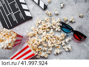 A banner for the film industry. A movie date. A movie camera, 3D glasses, popcorn in striped cups on a stylish concrete gray background. The premiere of the film. (2024 год). Стоковое фото, фотограф Photojuli / Фотобанк Лори