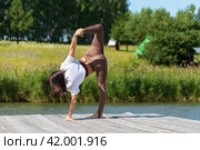 Slender woman practicing yoga, performing the Ardha Chandrasana exercise, a variation of the crescent pose, training on a summer morning on a wooden pier near the lake. Стоковое фото, фотограф Сергей Чайко / Фотобанк Лори