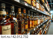Whiskey bottles on the shelves of a liquor Store. Advertising banner. Стоковое AI-изображение, AI-художник Ирина Ручушкина / Фотобанк Лори