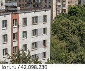 В жаркий летний день человек загорает, высунув ноги в распахнутое окно многоэтажного жилого дома высоко над землей (2023 год). Редакционное фото, фотограф Наталья Николаева / Фотобанк Лори