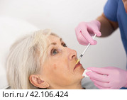 Unrecognizable beautician performing procedure of injection biorevitalization to elderly woman for alignment of facial asymmetry in esthetic clinic. Стоковое фото, фотограф Яков Филимонов / Фотобанк Лори