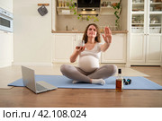 Fitness during pregnancy and abstinence from drinking alcohol, prepare for childbirth. A pregnant woman at a sports training session at home shows a stop gesture as a sign of giving up alcohol. Стоковое фото, фотограф Андрей Журавлев / Фотобанк Лори