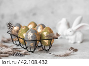 Stylish beautiful Easter eggs with golden potali coating and Easter bunny on a gray background. The concept of happy Easter 2024. Стоковое фото, фотограф Photojuli / Фотобанк Лори