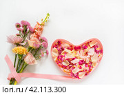 Bouquet of fresh flowers with roses, carnations and chrysanthemums with pink ribbon in shape of heart filled with rose petals. Romantic greetings on Valentine's Day, March 8 or Birthday. Стоковое фото, фотограф Виктория Катьянова / Фотобанк Лори